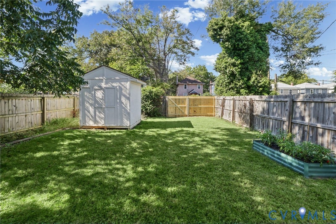 Expansive backyard featuring a manicured lawn, full perimeter fencing, storage shed, and a raised garden bed