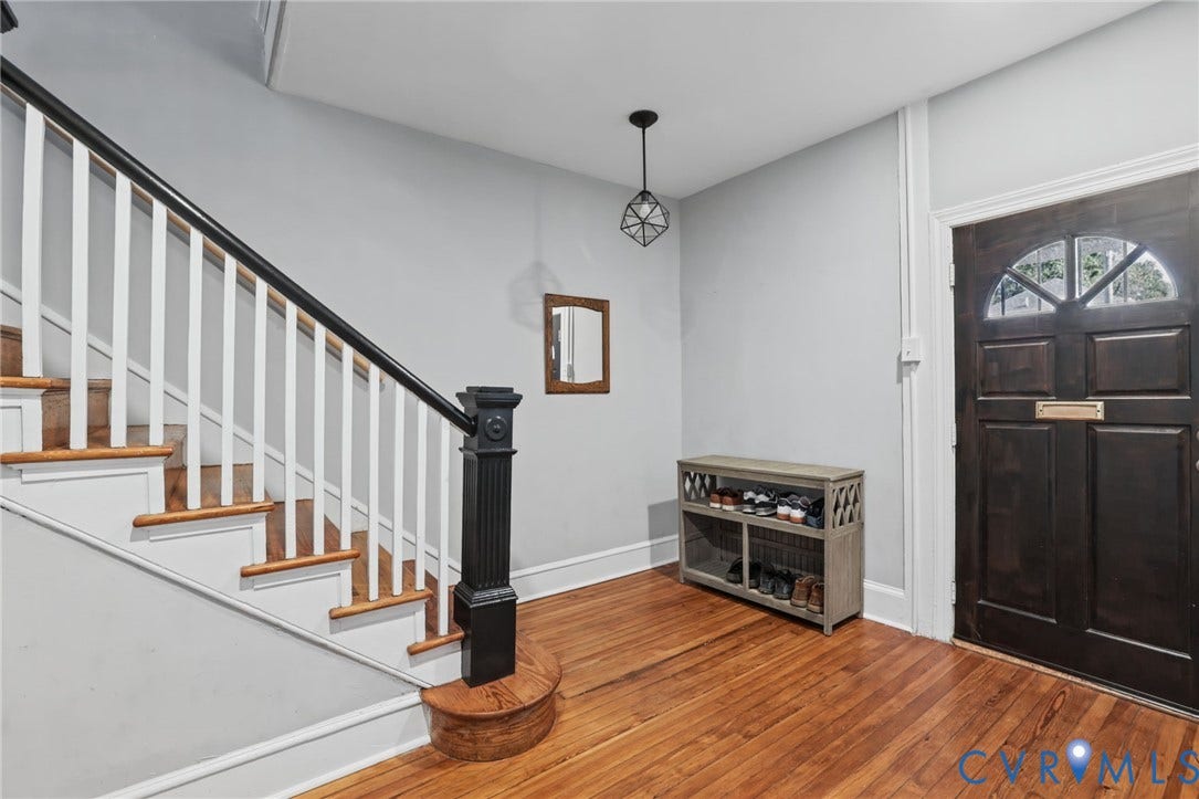 Hardwood flooring throughout, a dark wood entry door with leaded glass, a wood staircase with white risers, and a contemporary pendant light fixture