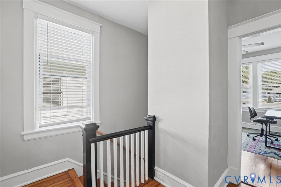 Hardwood flooring, painted banister, bright window with blinds, and white trim throughout