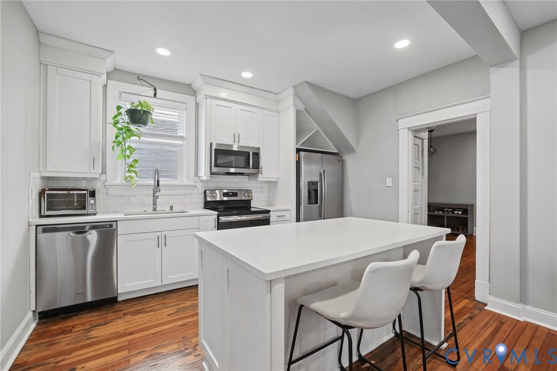 White shaker cabinetry, stainless steel appliances, solid surface countertops, wood-finish flooring, and recessed lighting