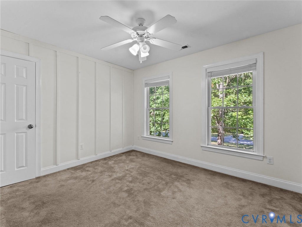 Neutral tone carpeted flooring, two paneled windows, a ceiling fan, and painted paneling detail