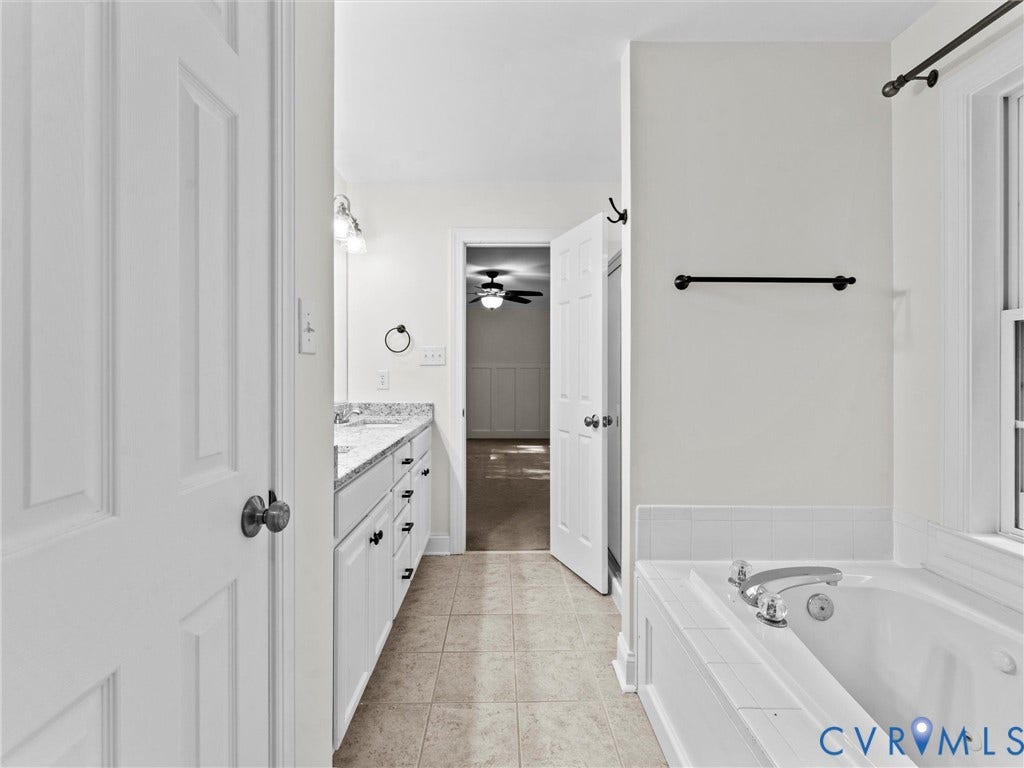 Dual vanity with granite countertop and white cabinetry, a built-in tub with tile surround, and tile flooring