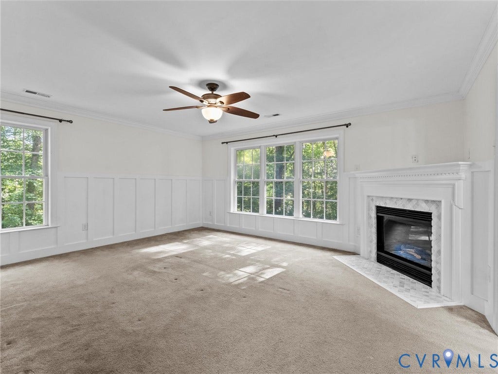 Fireplace with a white mantel and marble-look tile surround, large windows, ceiling fan with light fixture, and panel accent wall