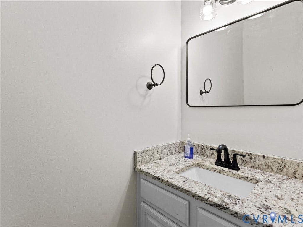 Modern bathroom vanity featuring a speckled stone countertop, undermount sink, matte black faucet, and framed mirror with integrated lighting
