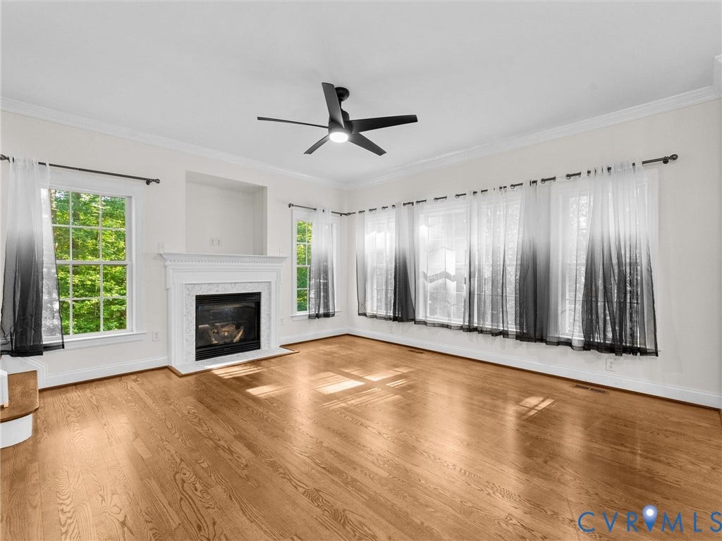 Hardwood flooring, fireplace with mantel, recessed wall niche, multiple large windows, and a ceiling fan