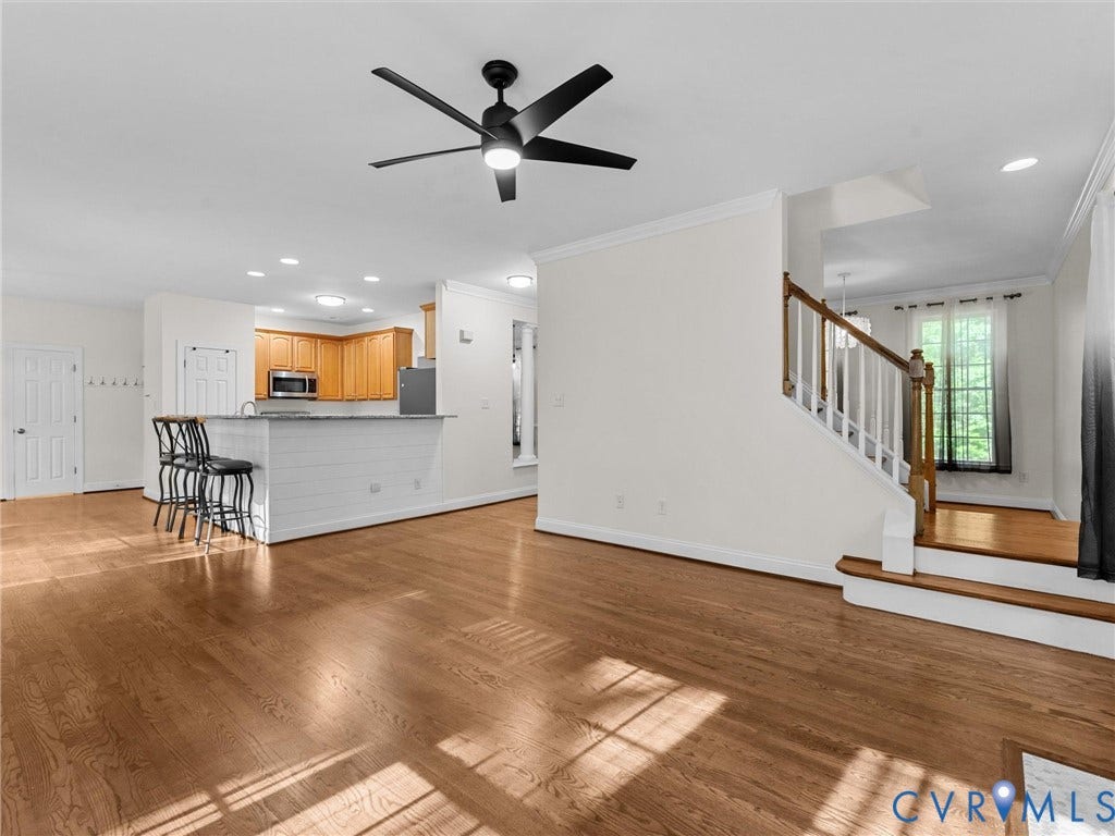 Hardwood flooring throughout, a ceiling fan with integrated lighting, recessed lighting, a staircase with wood newel posts, and a breakfast bar with shiplap detailing