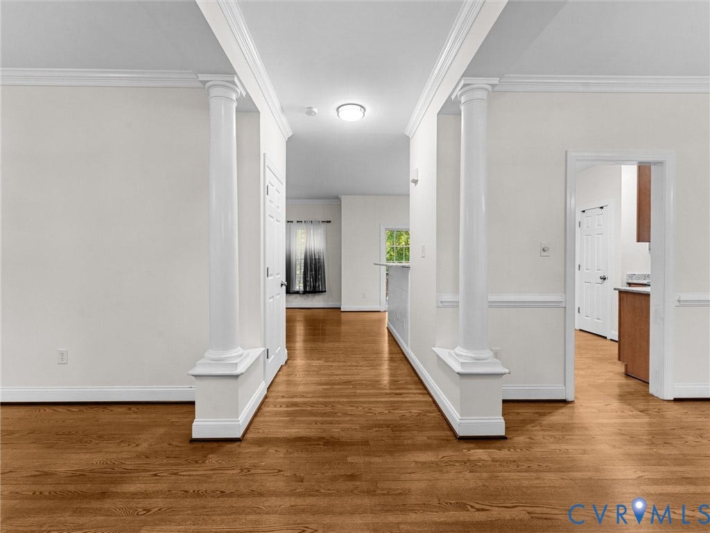 Wood-finish flooring with white baseboards, crown molding, and decorative columns