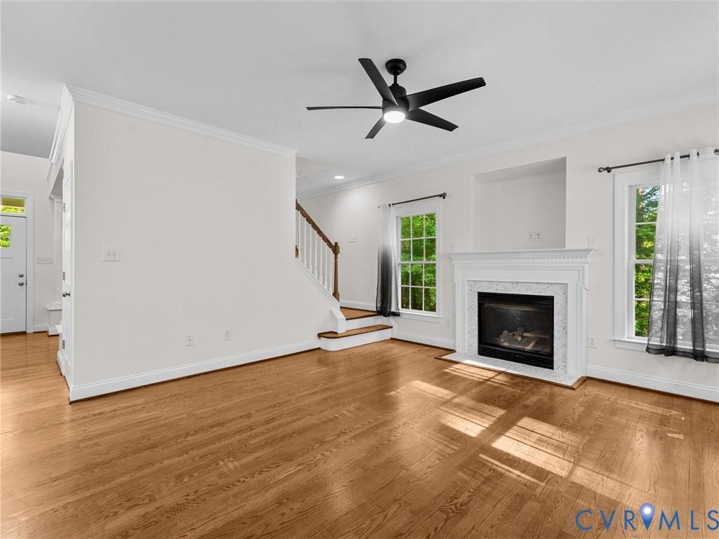 Hardwood flooring, white fireplace with a decorative mantel, black ceiling fan with integrated lighting, white trim and crown molding, and a staircase with white balusters