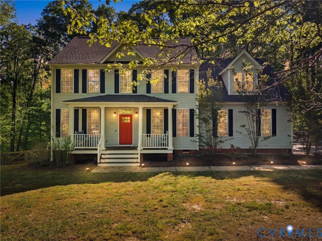 Traditional-style residence featuring light-colored siding, a covered front porch with white railings, a contrasting red entry door, and dark shutters on multiple windows