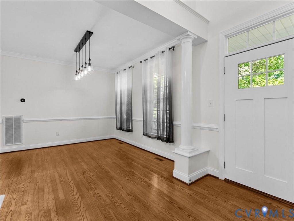 Hardwood flooring, decorative column, contemporary chandelier, craftsman-style entry door with transom window, and wainscoting