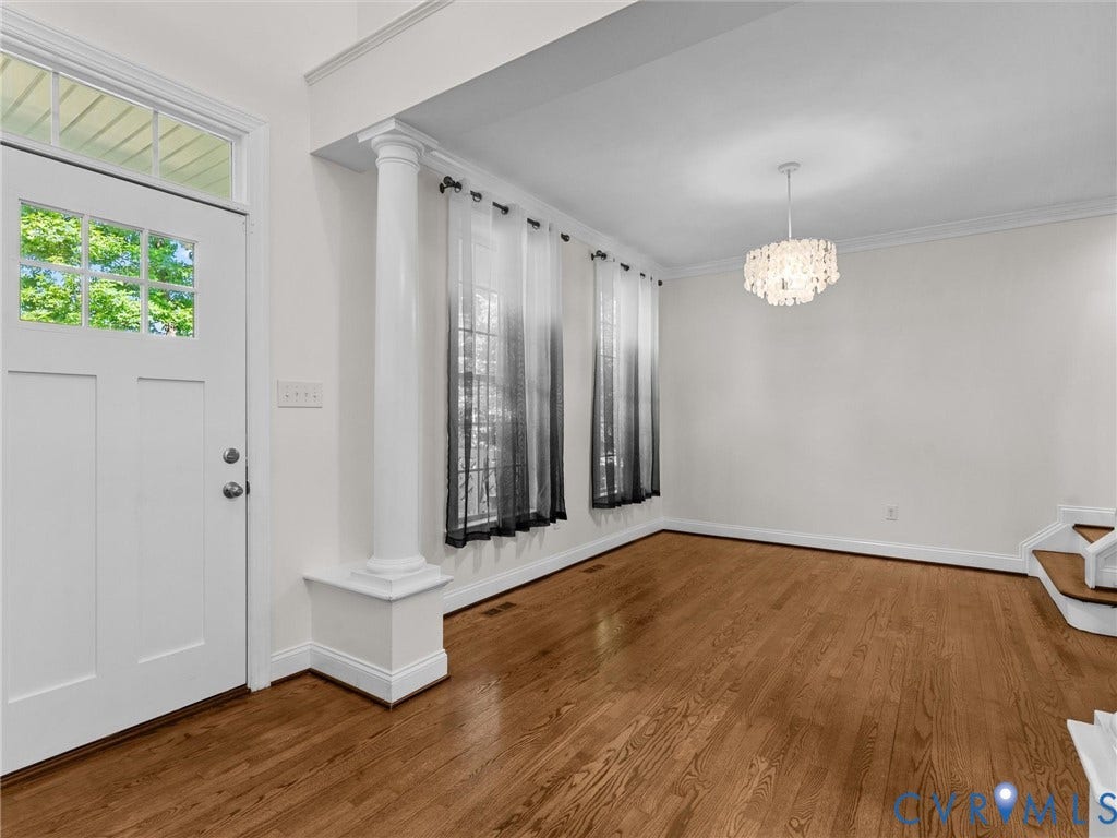 Hardwood flooring, decorative chandelier, white paneled door with glass inserts, architectural columns, and crown molding