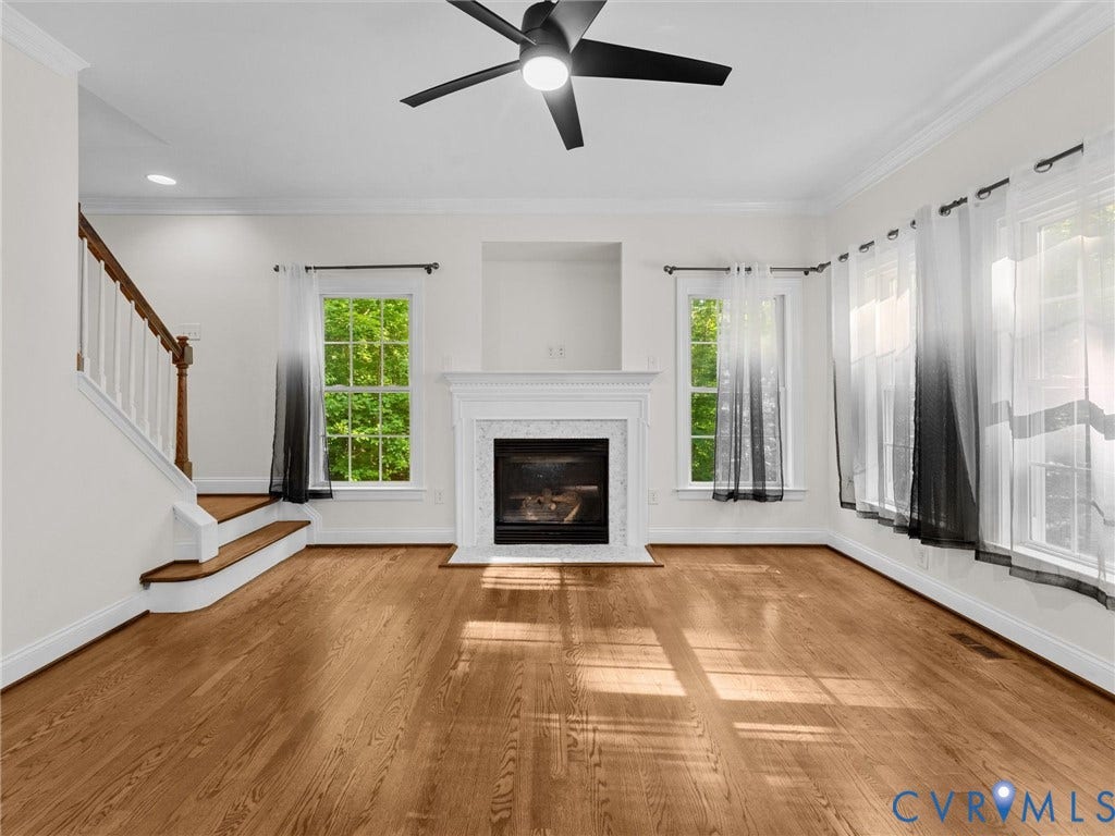 Hardwood flooring throughout, white mantel fireplace with tile surround, crown molding, a ceiling fan, and a staircase with wood treads and white risers
