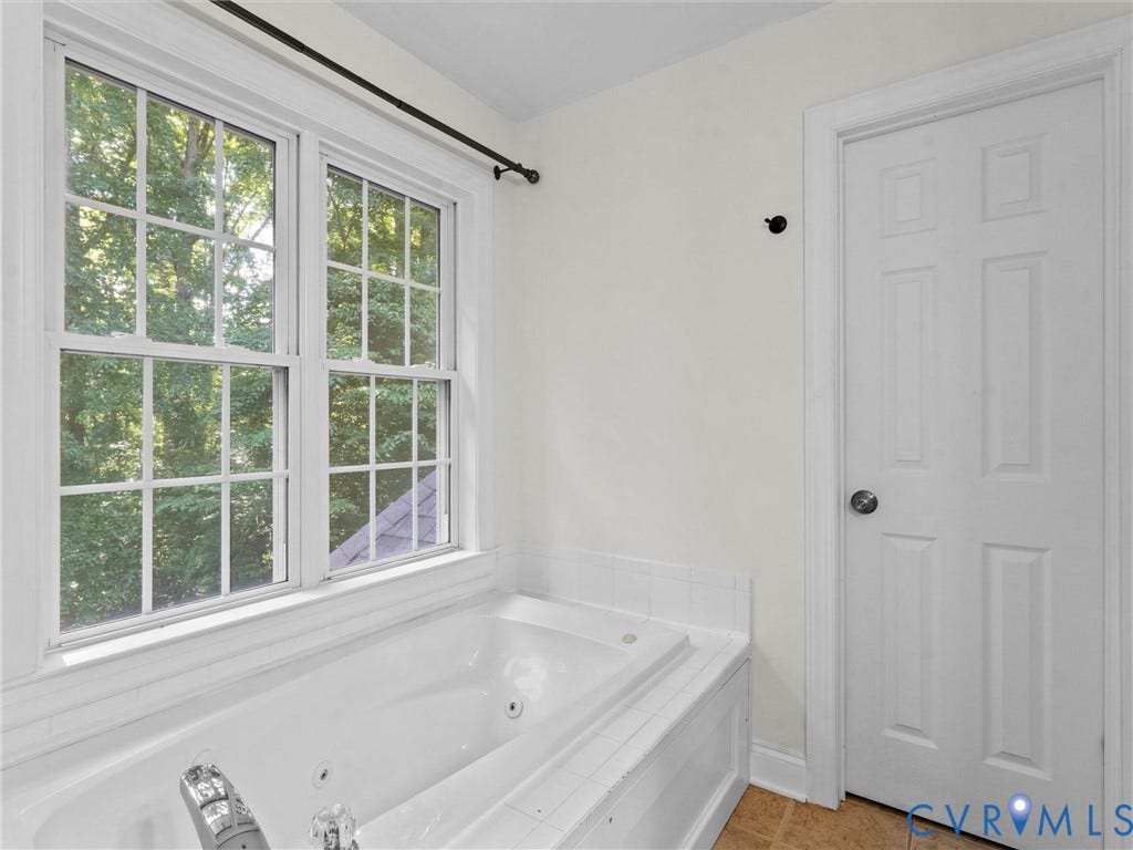 Jetted soaking tub with tile surround, framed by a double window with muntins, and a paneled door with a round knob