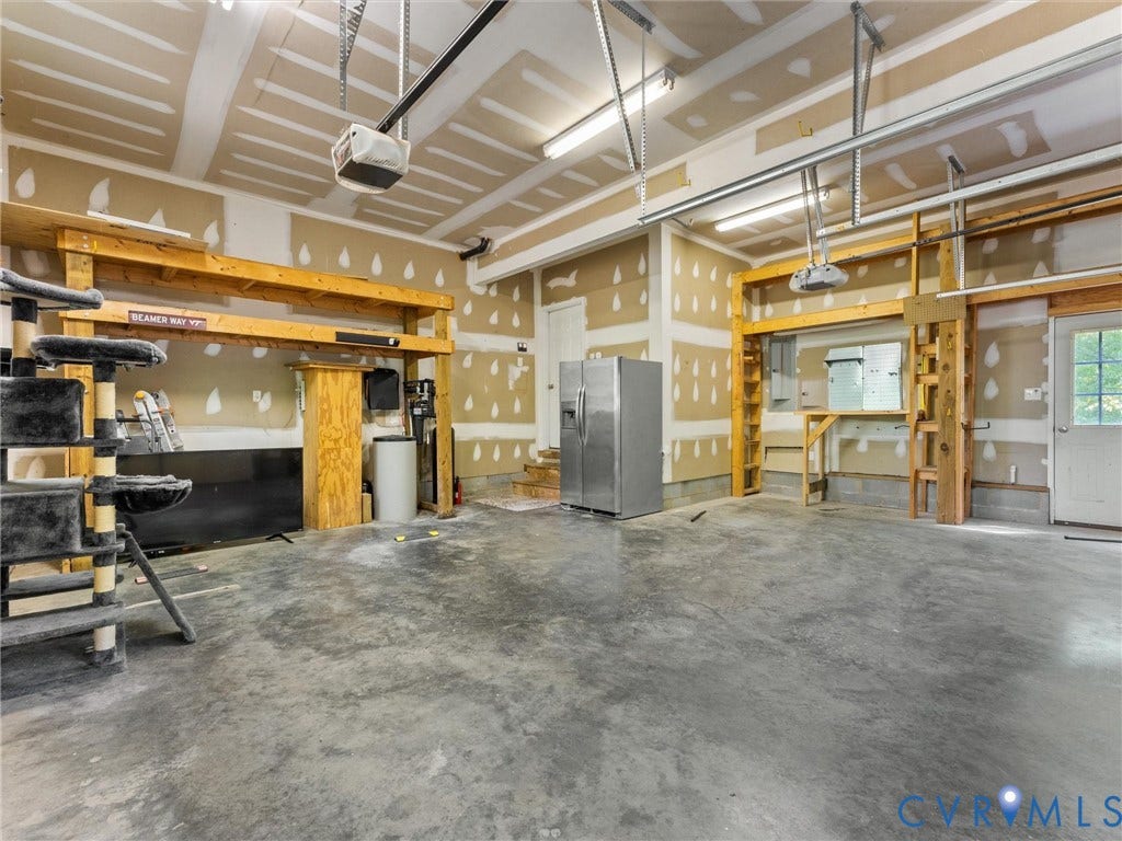 Spacious garage with concrete flooring, exposed ceiling joists, and built-in wooden shelving