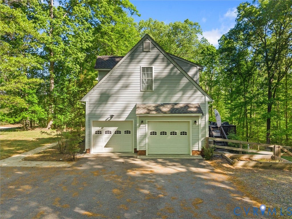 Two-car garage with individual doors, vertical siding, a second-story window, a sloped shingle roof, and surrounding mature trees