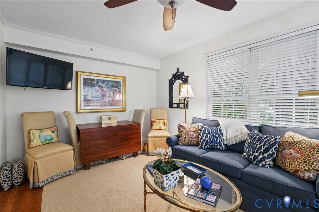 Living area featuring wood-finish flooring, ceiling-mounted paddle fan, and large windows with horizontal blinds