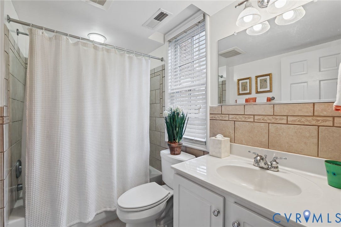 Bathroom featuring white cabinetry, integrated sink with chrome faucet, large vanity mirror, shower-tub combination with tiled surround, and window with built-in blinds