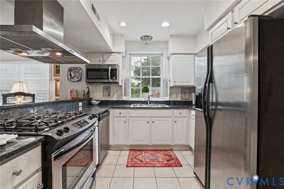 Kitchen featuring white shaker-style cabinetry, dark stone countertops, stainless steel appliances, a gas range with an overhead vent hood, and a multi-pane window