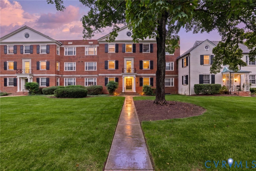 Colonial architecture featuring a brick facade, shuttered multi-pane windows, decorative pediments, and a central paved walkway