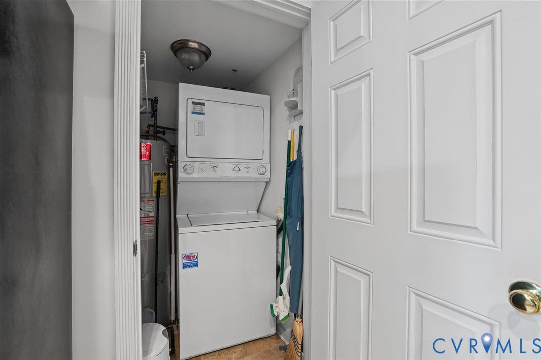 Utility closet featuring a stacked washer and dryer unit, integrated water heater, ceiling-mounted light fixture, and paneled door