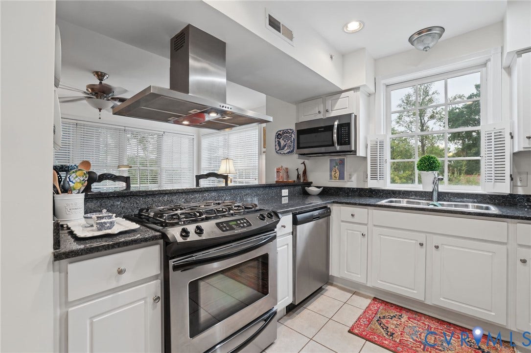 Kitchen featuring white cabinetry, dark stone countertops, stainless steel gas range with overhead hood, stainless steel dishwasher, and a multi-pane window