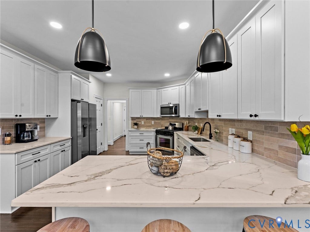 Expansive kitchen featuring a large island with a patterned countertop, white cabinetry with black hardware, and a tile backsplash