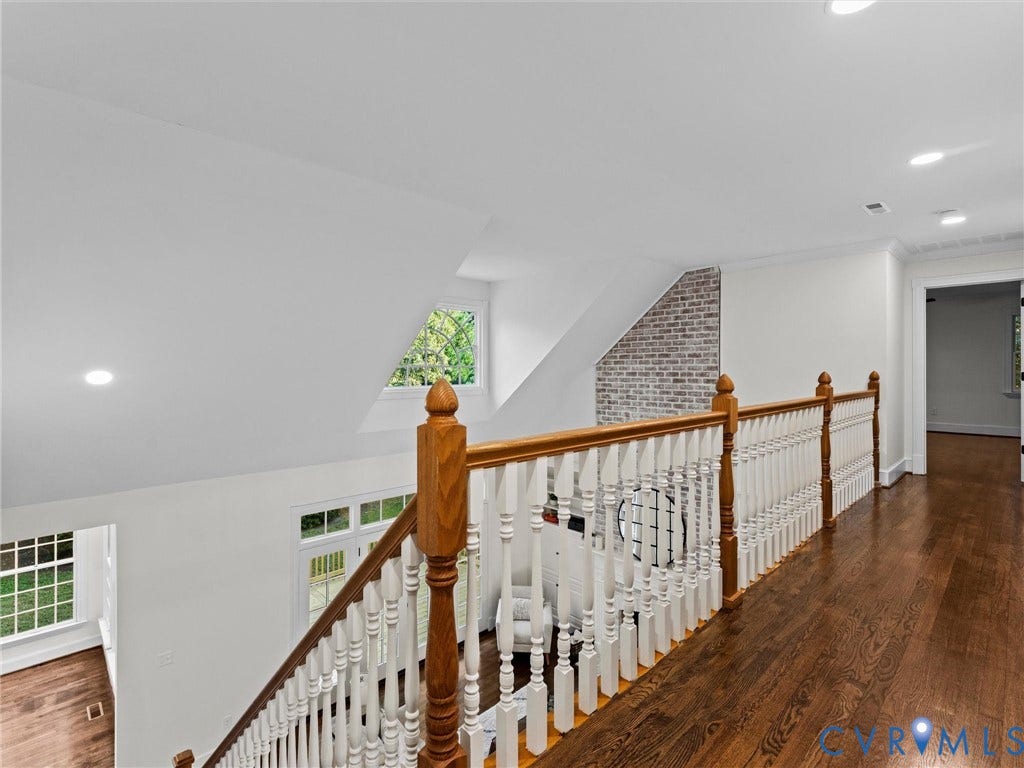 Hardwood flooring throughout the upper level, white baluster railing with wood-stained handrail, recessed lighting, and a brick accent wall