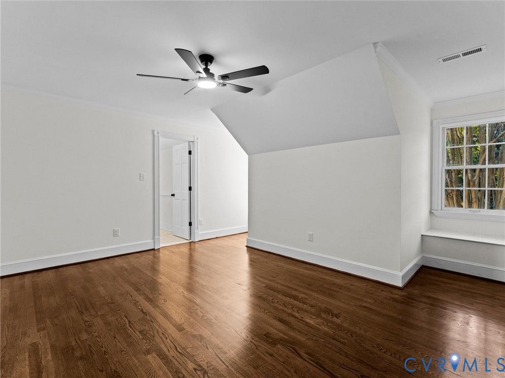 Hardwood flooring throughout, featuring a ceiling fan with integrated lighting, a built-in window bench, and a white paneled door