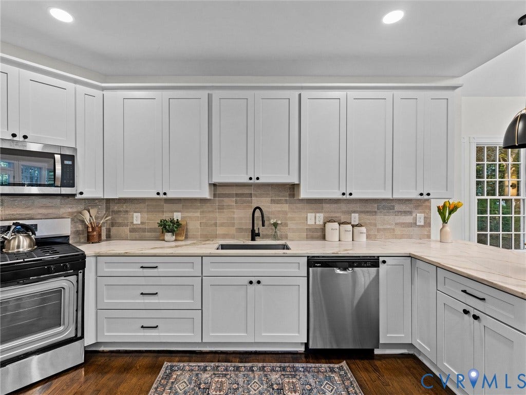 White shaker-style cabinetry with black hardware, stainless steel appliances, stone countertops, and a tiled backsplash