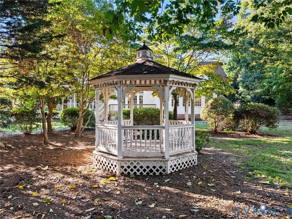 White octagonal gazebo with a dark shingled roof, surrounded by mature trees and shrubs