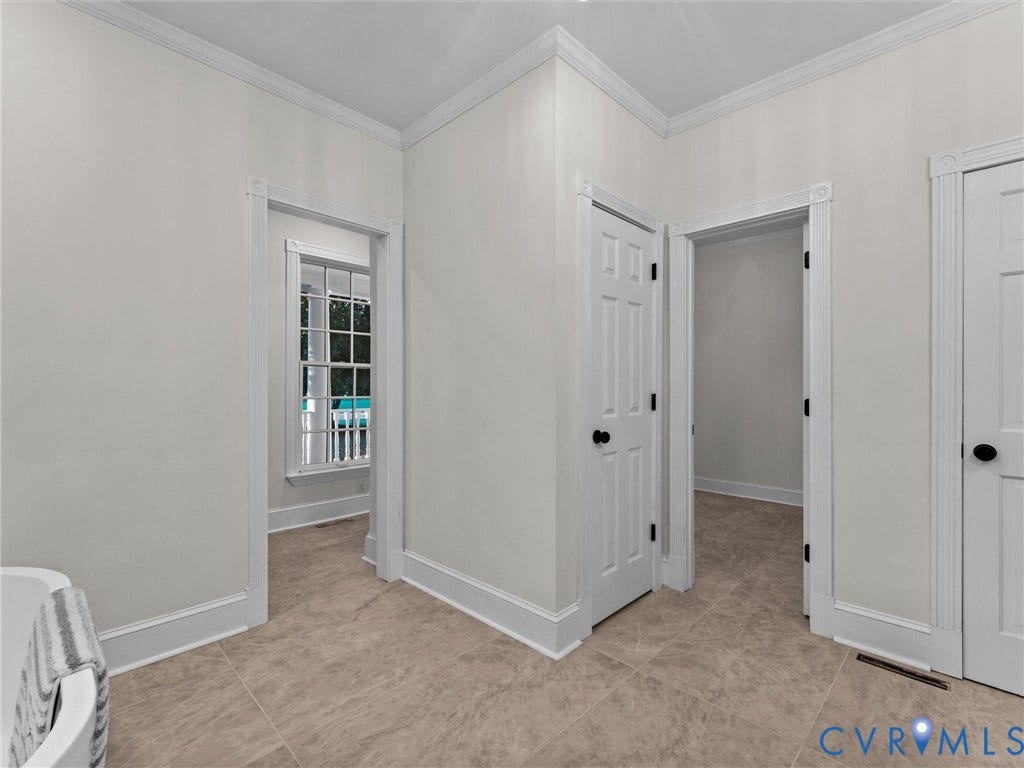 Bright corner bedroom showcasing neutral wall finishes, wood-finish flooring, and multiple white six-panel doors with black hardware