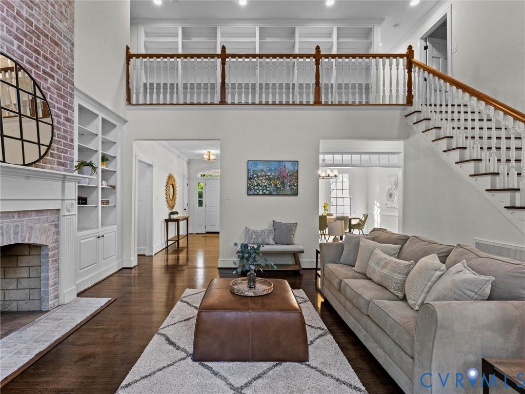 Two-story living area with dark wood-finish flooring, a brick fireplace, and built-in shelving