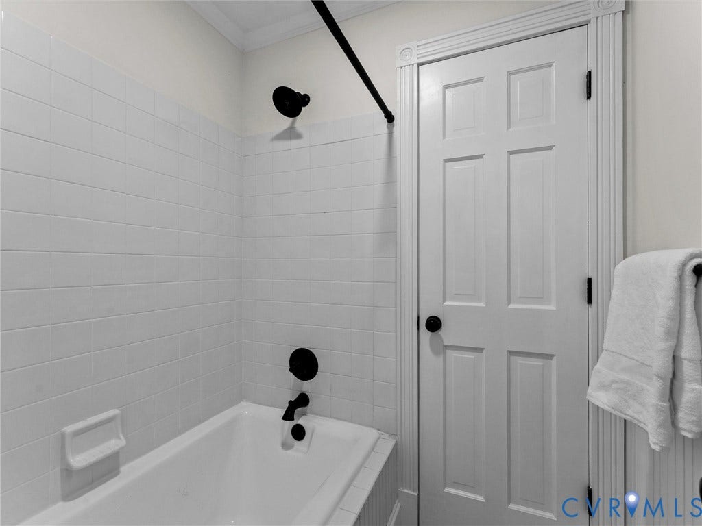 White subway tile surround, matte black shower fixtures, four-panel interior door, and decorative door trim