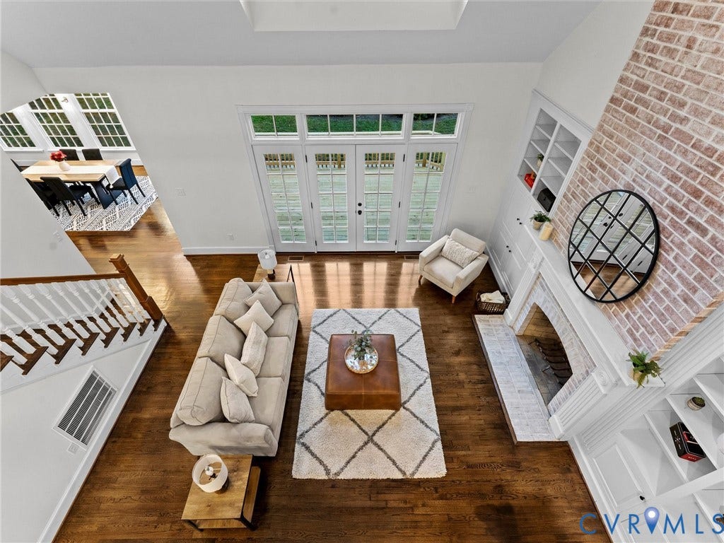 Wood-finish flooring, white brick fireplace with mantel, built-in shelving, staircase with white spindles, and double French doors with transom windows