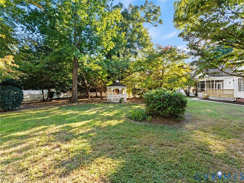 Expansive grassy area with mature trees, a white gazebo, privacy fencing, and a screened porch with a ramp