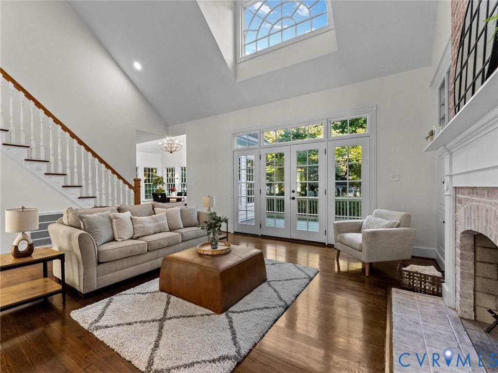 Hardwood flooring, vaulted ceiling, large arched window, double French doors, and a brick-surround fireplace with a white mantel