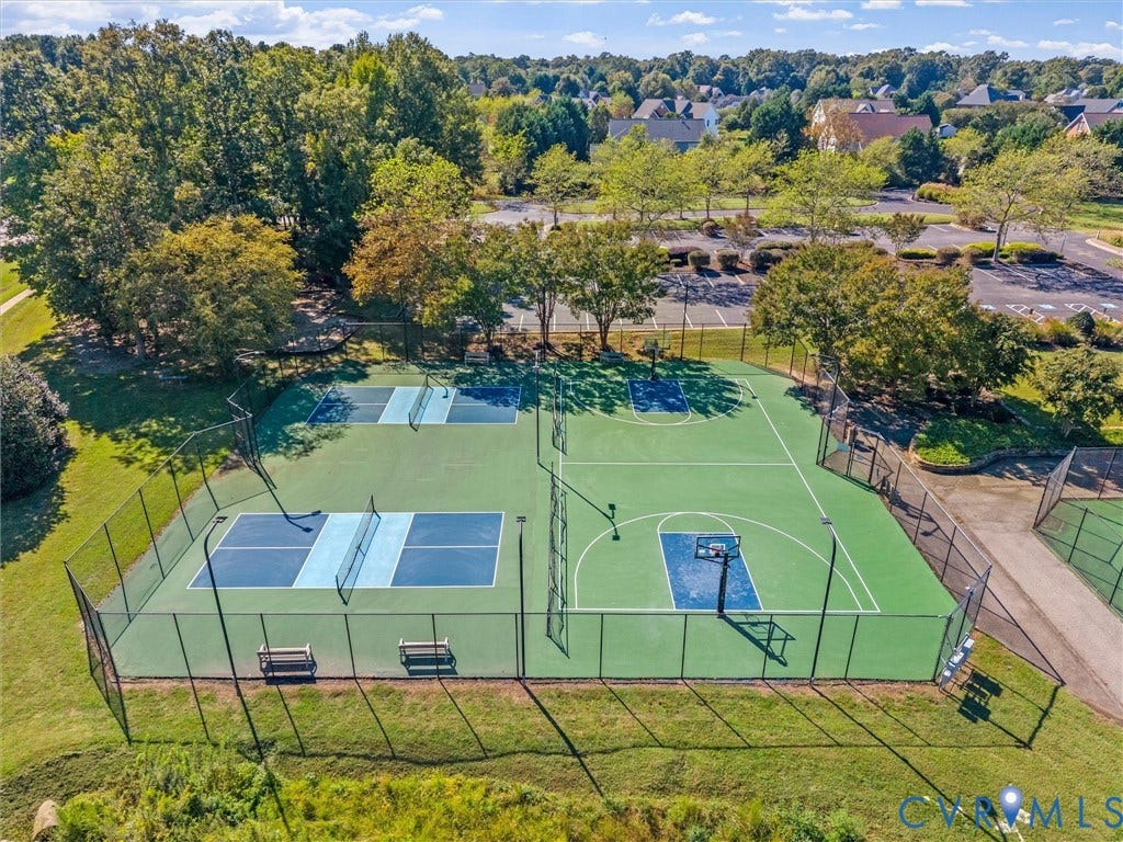 Fenced recreation area featuring a basketball court, two pickleball courts, and spectator benches