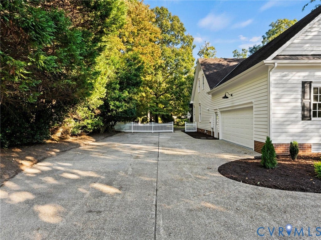 Concrete driveway leading to a two-car garage with white siding, black shutters, and a white picket fence