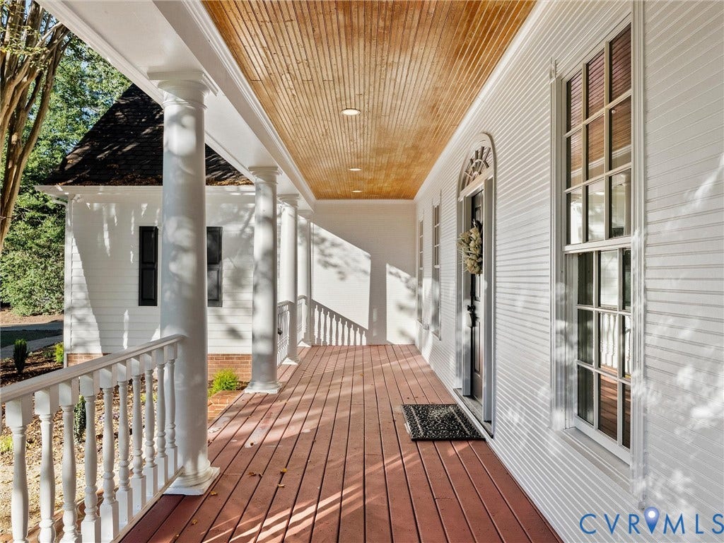 Expansive front porch featuring a wood-finish floor, white balustrade railing, and classical columns