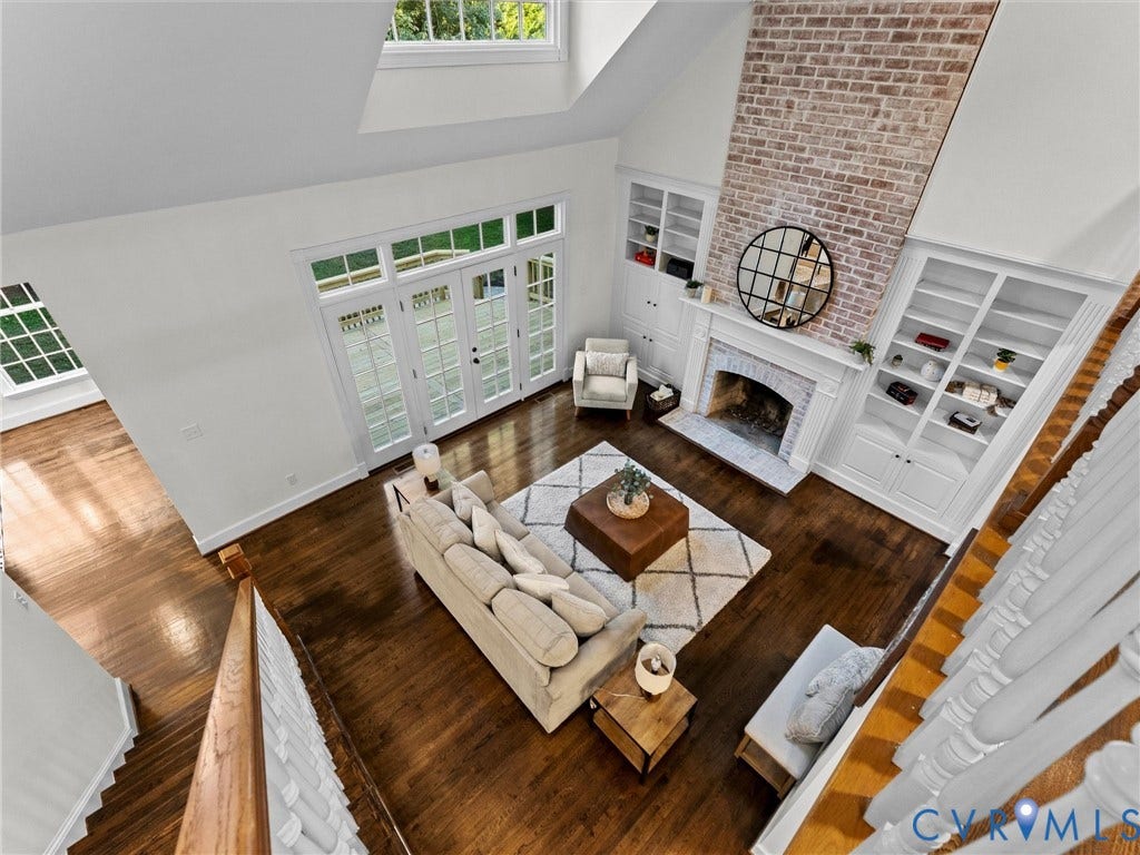 Vaulted ceiling with skylight, extensive wood-finish flooring, brick-faced fireplace with hearth, built-in shelving, and transom windows