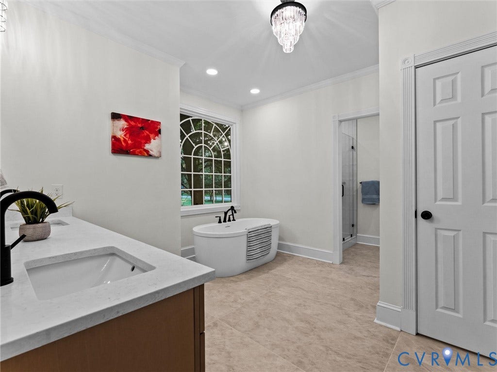 Freestanding soaking tub with black fixtures, custom vanity with undermount sink, quartz countertop, and black faucet, a walk-in shower with clear glass enclosure, and decorative tile flooring