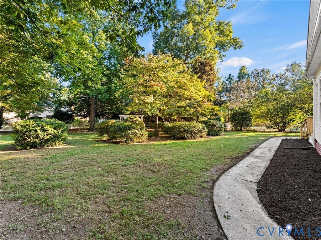 Expansive grassy yard with mature trees and established shrubbery, featuring a concrete pathway and mulched planting beds