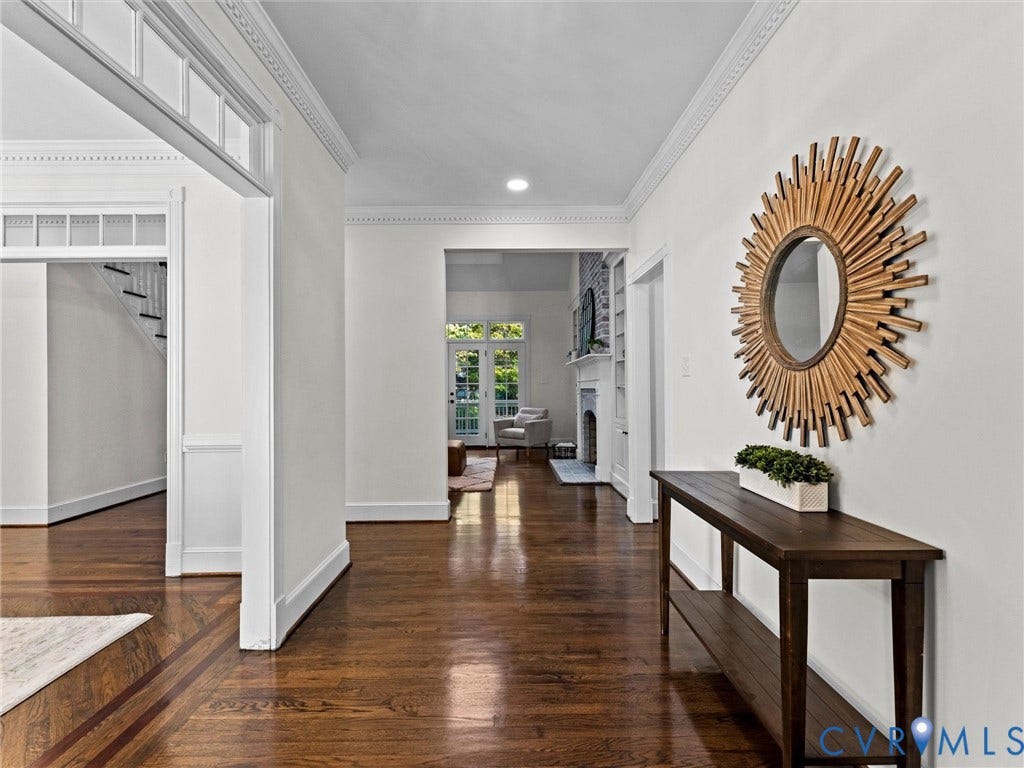 Hardwood flooring with decorative inlay, crown molding, transom window architectural detailing, and painted white walls