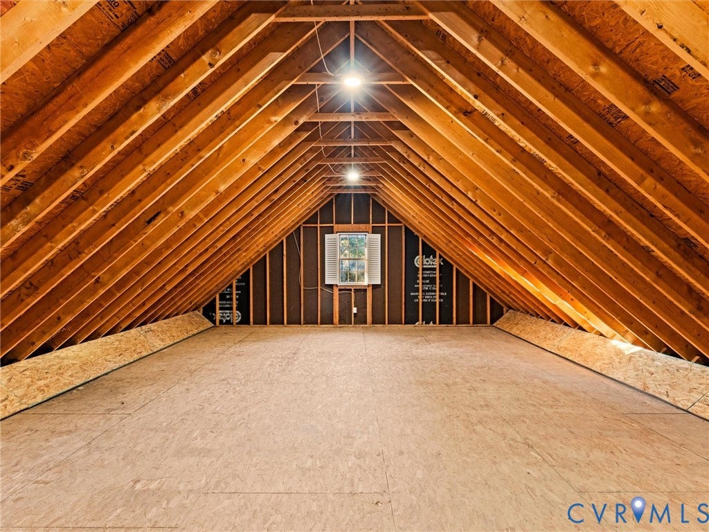 Spacious unfinished attic space featuring exposed wood framing, plywood flooring, and a central window