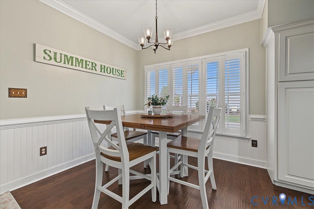 Dining area featuring wood-finish flooring, white beadboard wainscoting, crown molding, multi-panel window shutters, and a central chandelier