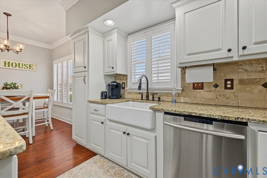 Kitchen featuring white shaker-style cabinetry, stone-finish countertops, apron-front farmhouse sink with a matte black faucet, tile backsplash, and wood-finish flooring
