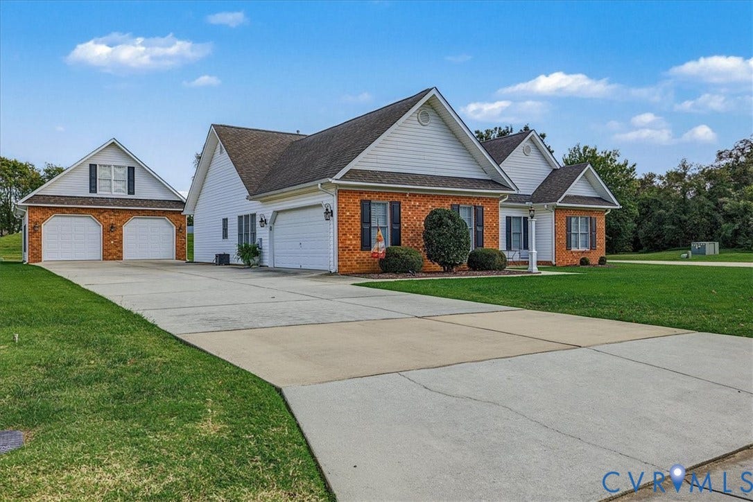 Brick and vinyl siding exterior featuring a multi-gabled roofline, three-car garage capacity, shuttered windows, and an expansive concrete driveway