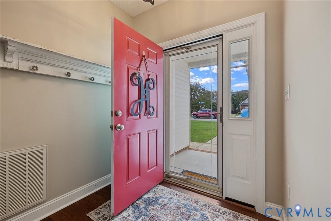 Entryway featuring a solid-core red front door, glass storm door with integrated screen, side light, and built-in wall-mounted coat rack