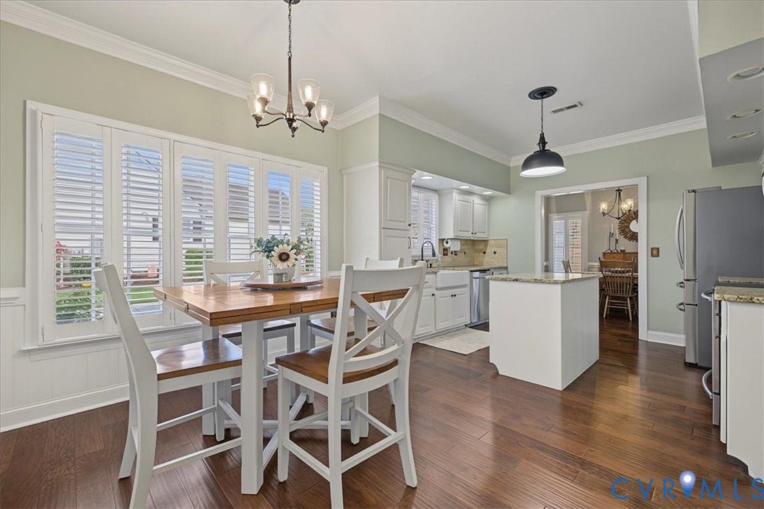 Kitchen featuring wood-finish flooring, white cabinetry, a center island with a stone-surface countertop, and plantation shutters on expansive windows