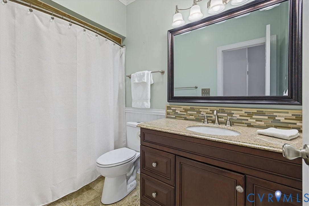Dark wood-finish cabinetry, stone-composite countertop with an integrated oval sink, multi-tonal linear tile backsplash, and a wide-framed vanity mirror